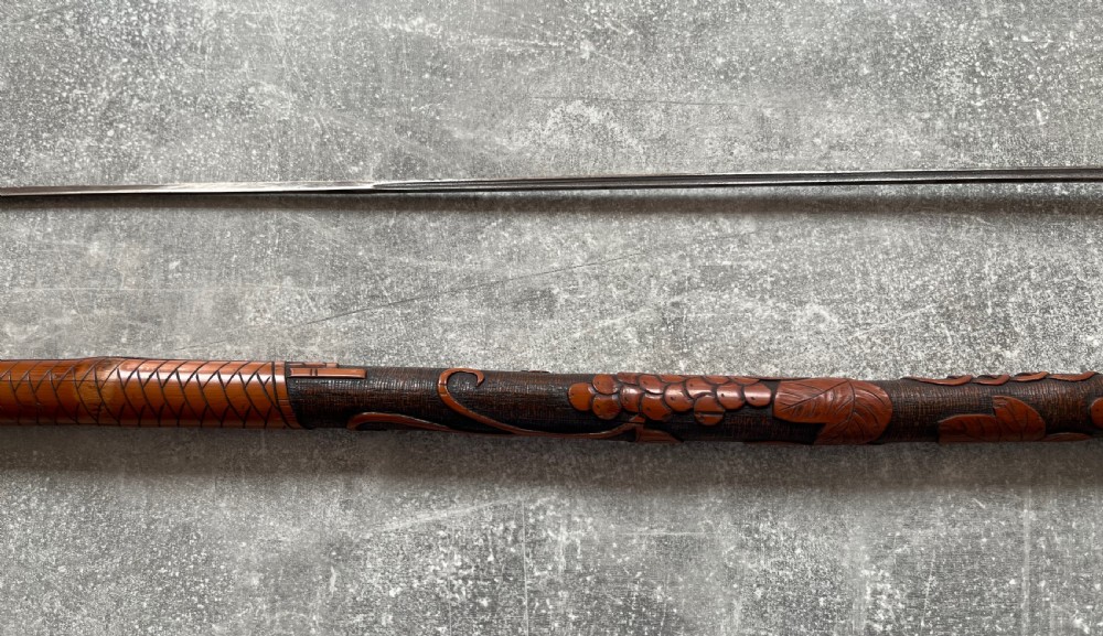 An antique East Asian carved bamboo sword stick shown unsheathed to reveal a long slender steel blade alongside its carved wooden shaft with brass fittings. View VII