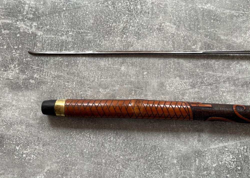 An antique East Asian carved bamboo sword stick shown unsheathed to reveal a long slender steel blade alongside its carved wooden shaft with brass fittings. View VIII