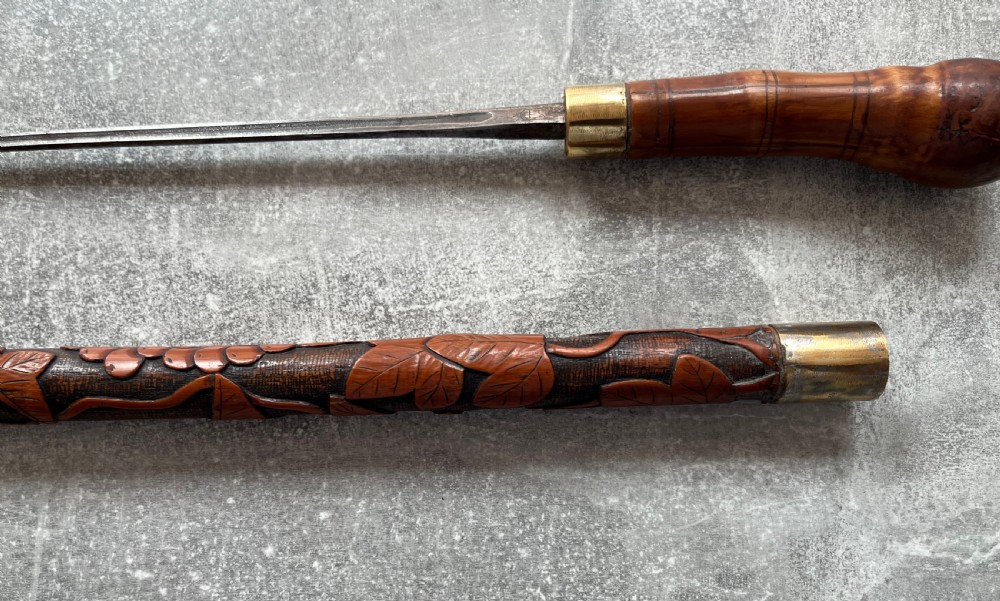 An antique East Asian carved bamboo sword stick shown unsheathed to reveal a long slender steel blade alongside its carved wooden shaft with brass fittings. View IX