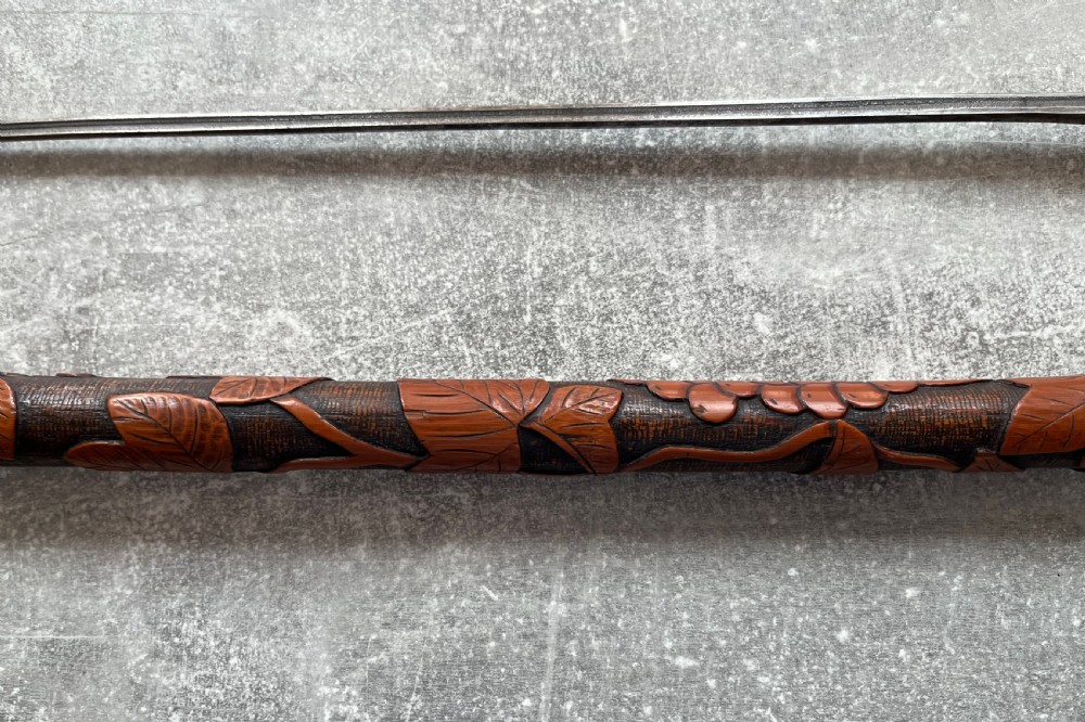 An antique East Asian carved bamboo sword stick shown unsheathed to reveal a long slender steel blade alongside its carved wooden shaft with brass fittings. View X