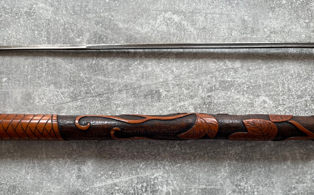 An antique East Asian carved bamboo sword stick shown unsheathed to reveal a long slender steel blade alongside its carved wooden shaft with brass fittings. View XI