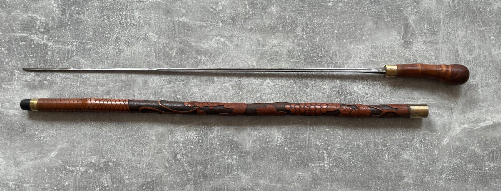 An antique East Asian carved bamboo sword stick shown unsheathed to reveal a long slender steel blade alongside its carved wooden shaft with brass fittings. View XIV