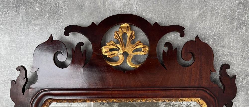 An upright rectangular wall mirror framed in dark mahogany with scroll-cut fretwork borders and a gilded carved motif at the top crest. View II