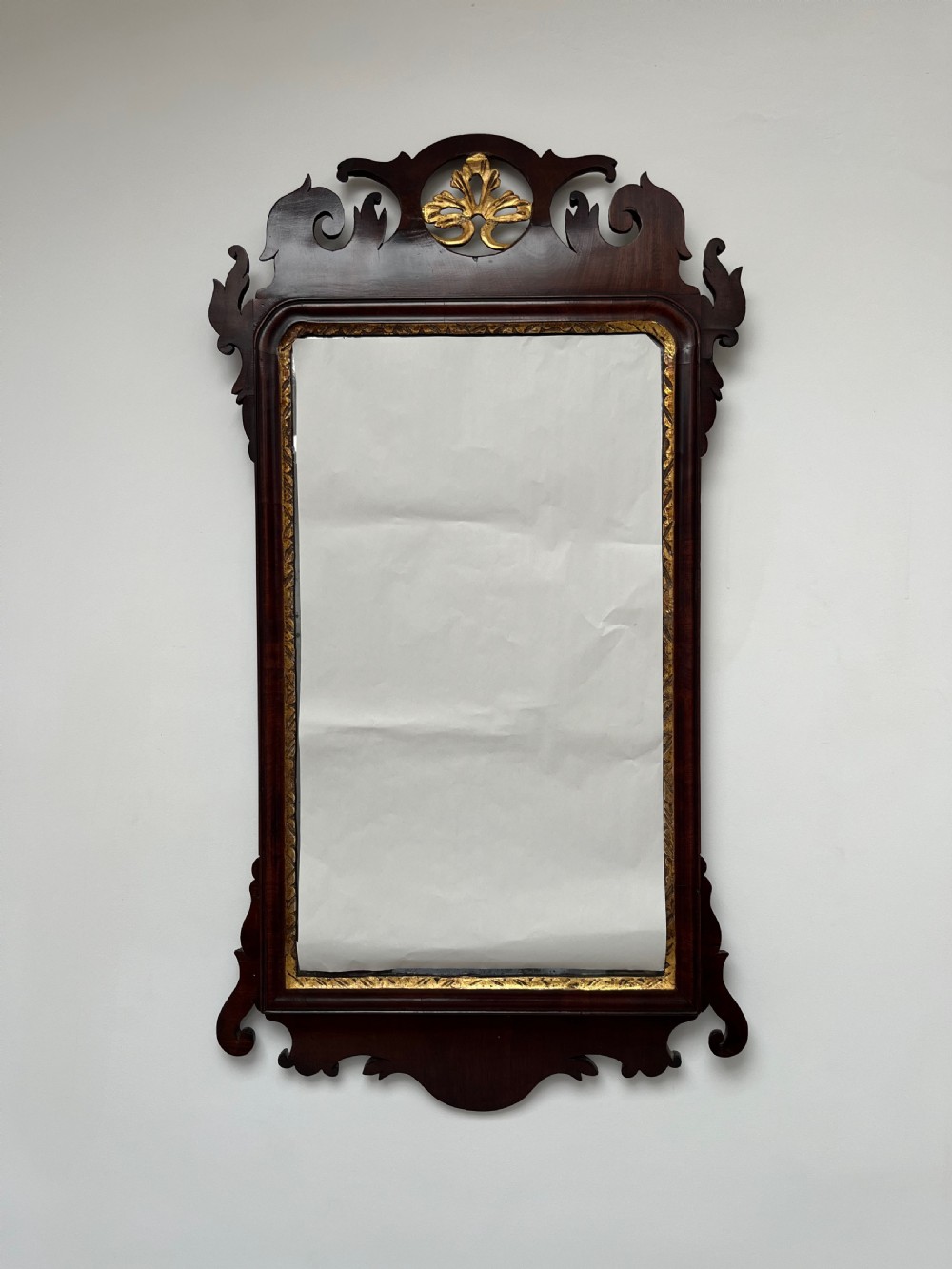 An upright rectangular wall mirror framed in dark mahogany with scroll-cut fretwork borders and a gilded carved motif at the top crest. View III