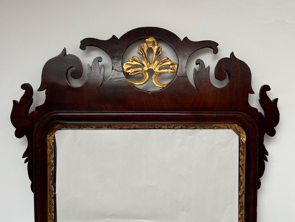 An upright rectangular wall mirror framed in dark mahogany with scroll-cut fretwork borders and a gilded carved motif at the top crest. View IV