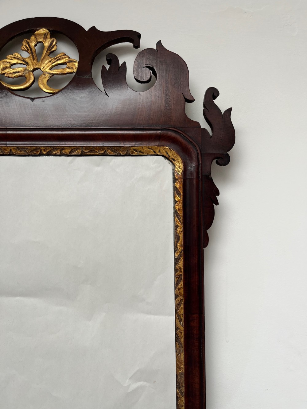 An upright rectangular wall mirror framed in dark mahogany with scroll-cut fretwork borders and a gilded carved motif at the top crest. View V