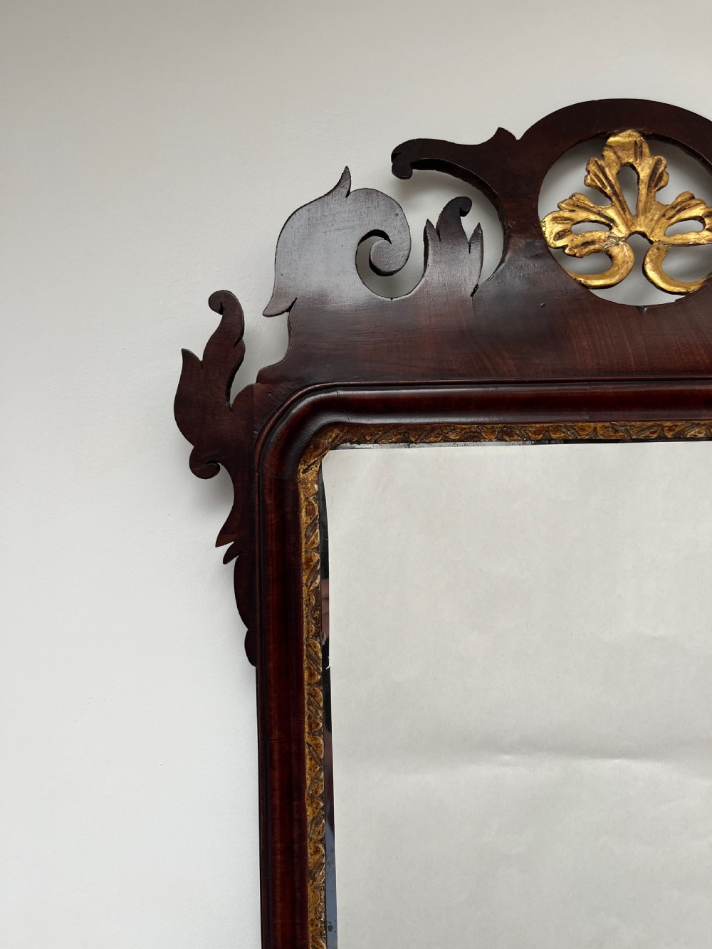 An upright rectangular wall mirror framed in dark mahogany with scroll-cut fretwork borders and a gilded carved motif at the top crest. View VI