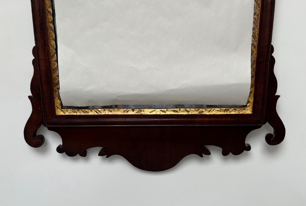 An upright rectangular wall mirror framed in dark mahogany with scroll-cut fretwork borders and a gilded carved motif at the top crest. View VII