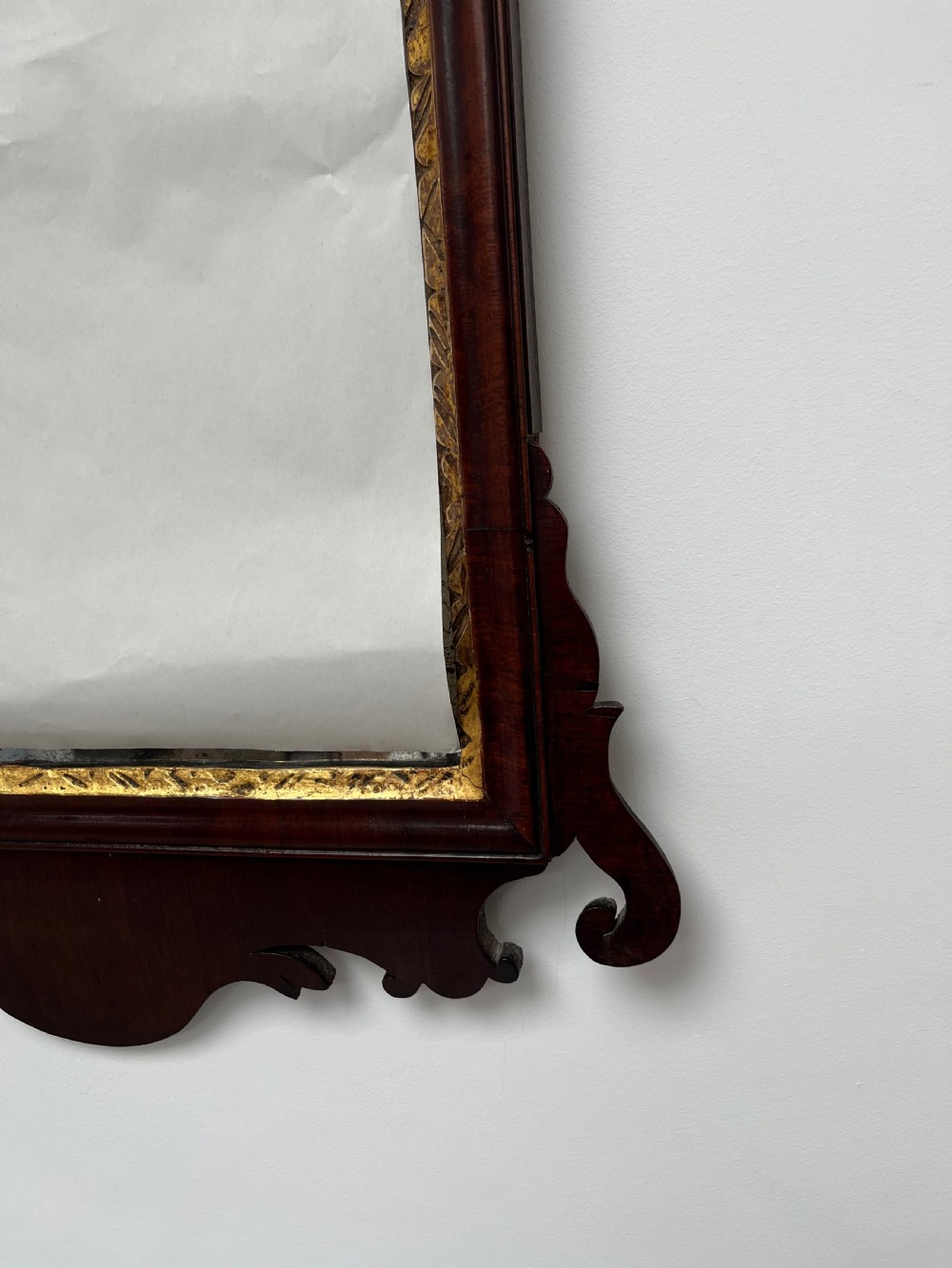 An upright rectangular wall mirror framed in dark mahogany with scroll-cut fretwork borders and a gilded carved motif at the top crest. View IX
