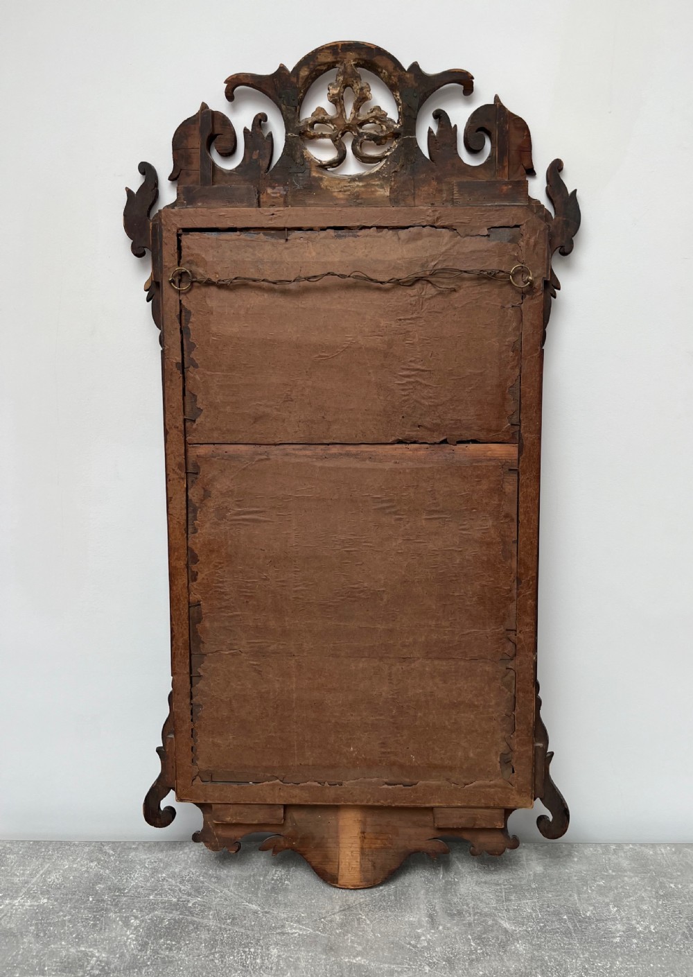 An upright rectangular wall mirror framed in dark mahogany with scroll-cut fretwork borders and a gilded carved motif at the top crest. View XIII