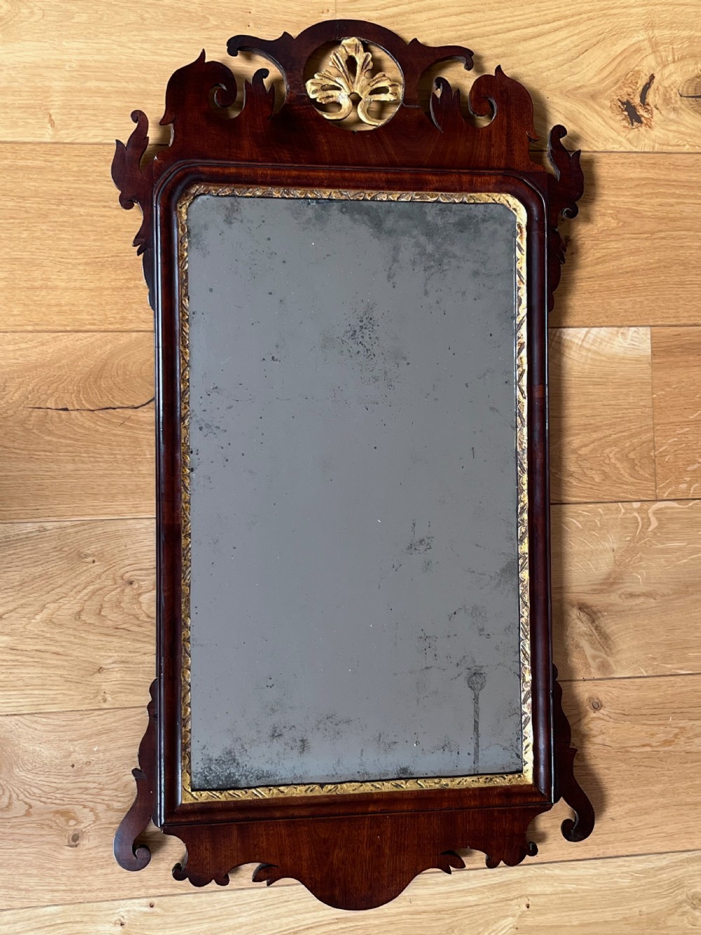An upright rectangular wall mirror framed in dark mahogany with scroll-cut fretwork borders and a gilded carved motif at the top crest. View XIV