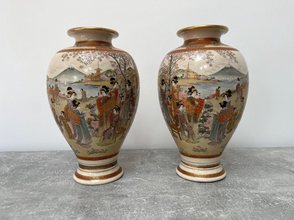 A pair of baluster-shaped Japanese Satsuma earthenware vases decorated with painted figures in landscapes under a crackled cream glaze with gilded borders.
