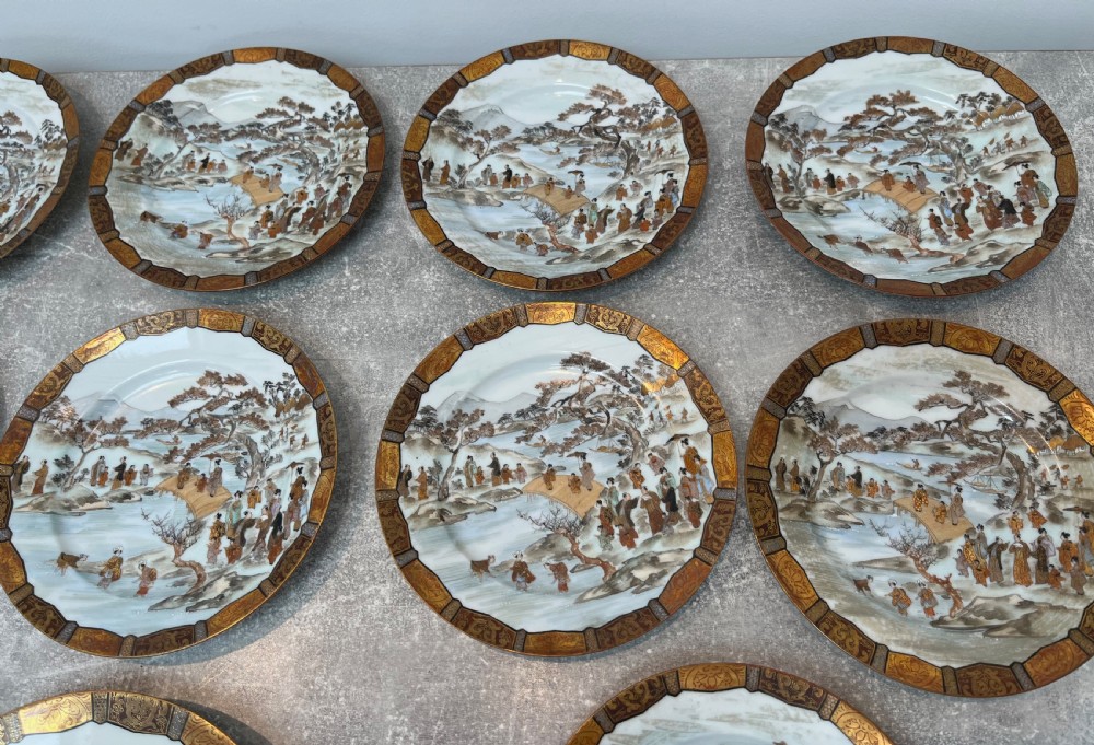 A set of twelve circular Japanese Satsuma earthenware plates featuring hand-painted landscape scenes with figures framed by wide gilded decorative borders. View III