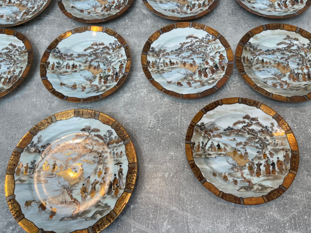 A set of twelve circular Japanese Satsuma earthenware plates featuring hand-painted landscape scenes with figures framed by wide gilded decorative borders. View IV