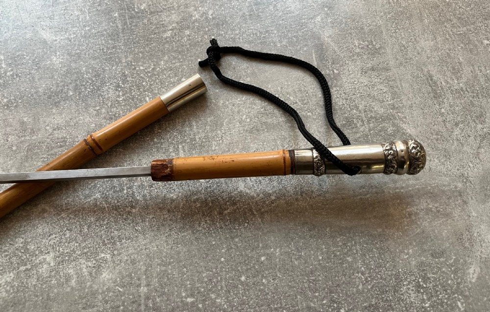 An early twentieth-century bamboo sword stick featuring an embossed silver pommel, a narrow steel blade, and a woven black wrist cord. View III