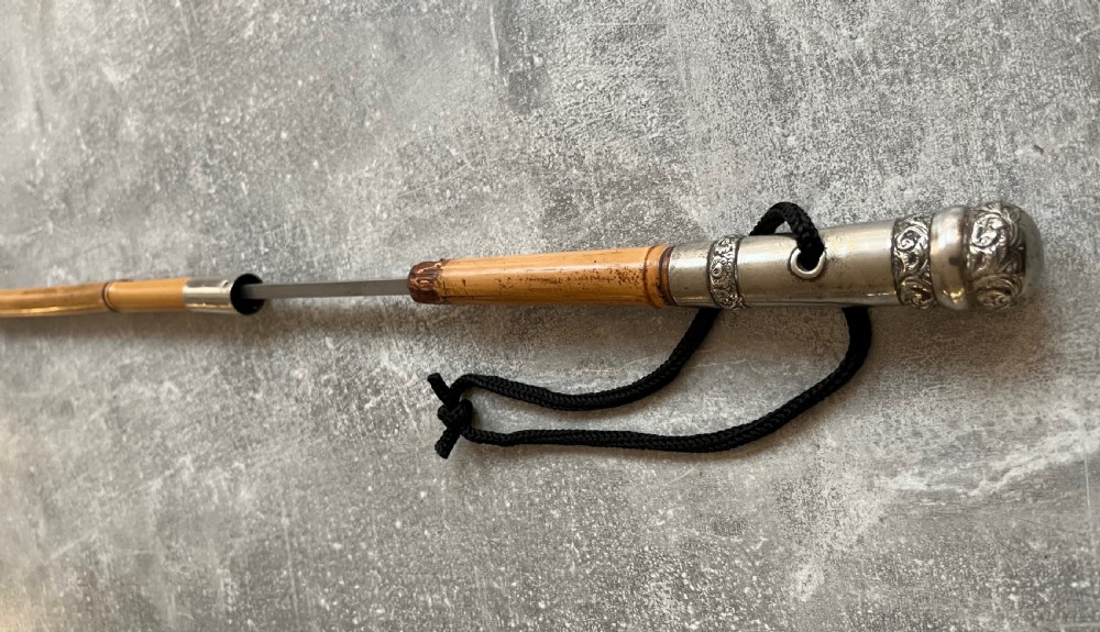An early twentieth-century bamboo sword stick featuring an embossed silver pommel, a narrow steel blade, and a woven black wrist cord. View VI