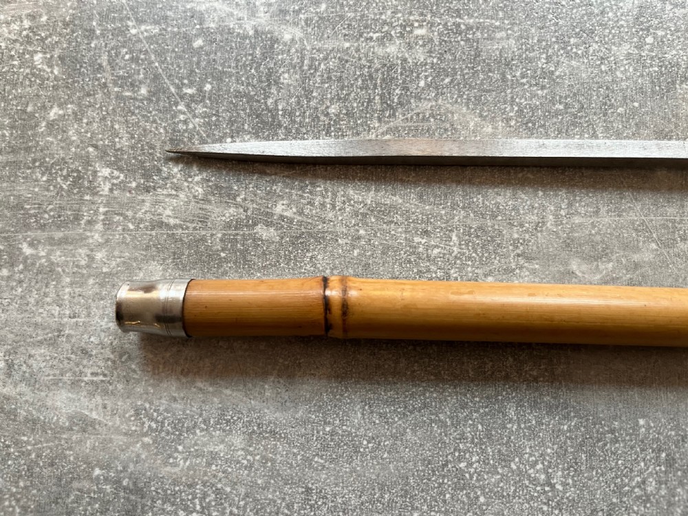 An early twentieth-century bamboo sword stick featuring an embossed silver pommel, a narrow steel blade, and a woven black wrist cord. View VII