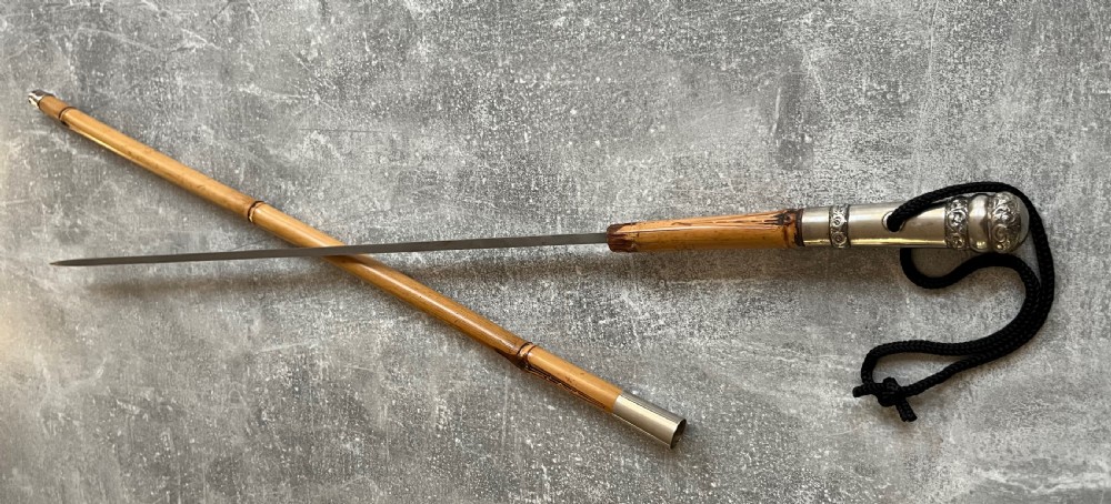 An early twentieth-century bamboo sword stick featuring an embossed silver pommel, a narrow steel blade, and a woven black wrist cord. View XI