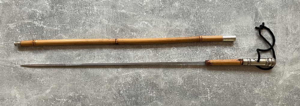 An early twentieth-century bamboo sword stick featuring an embossed silver pommel, a narrow steel blade, and a woven black wrist cord. View XII