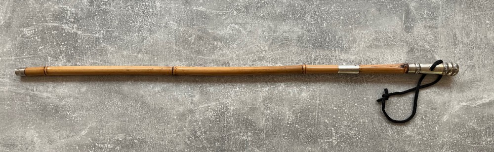 An early twentieth-century bamboo sword stick featuring an embossed silver pommel, a narrow steel blade, and a woven black wrist cord. View XIII
