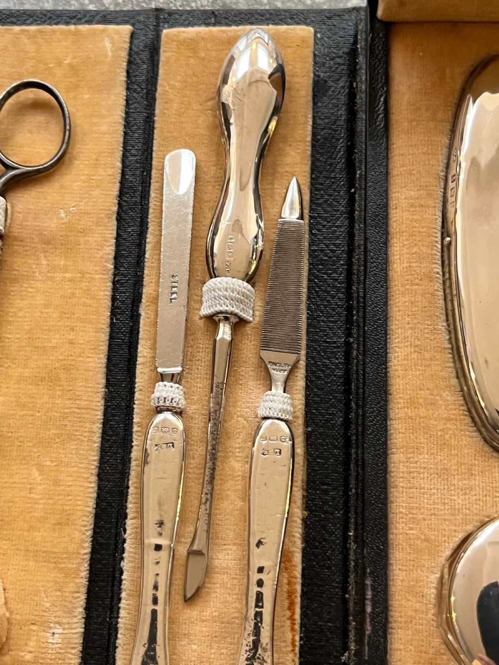 An open black folding leather case with velvet lining displaying a multi-piece antique silver manicure set including scissors, files, a nail buffer, and a small silver container. View VIII