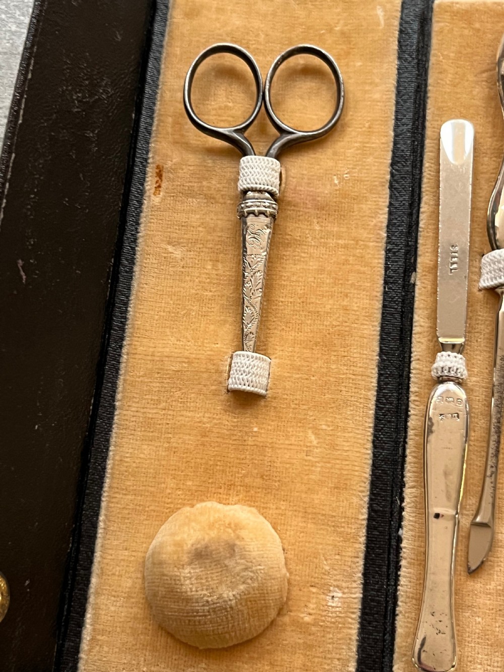 An open black folding leather case with velvet lining displaying a multi-piece antique silver manicure set including scissors, files, a nail buffer, and a small silver container. View IX