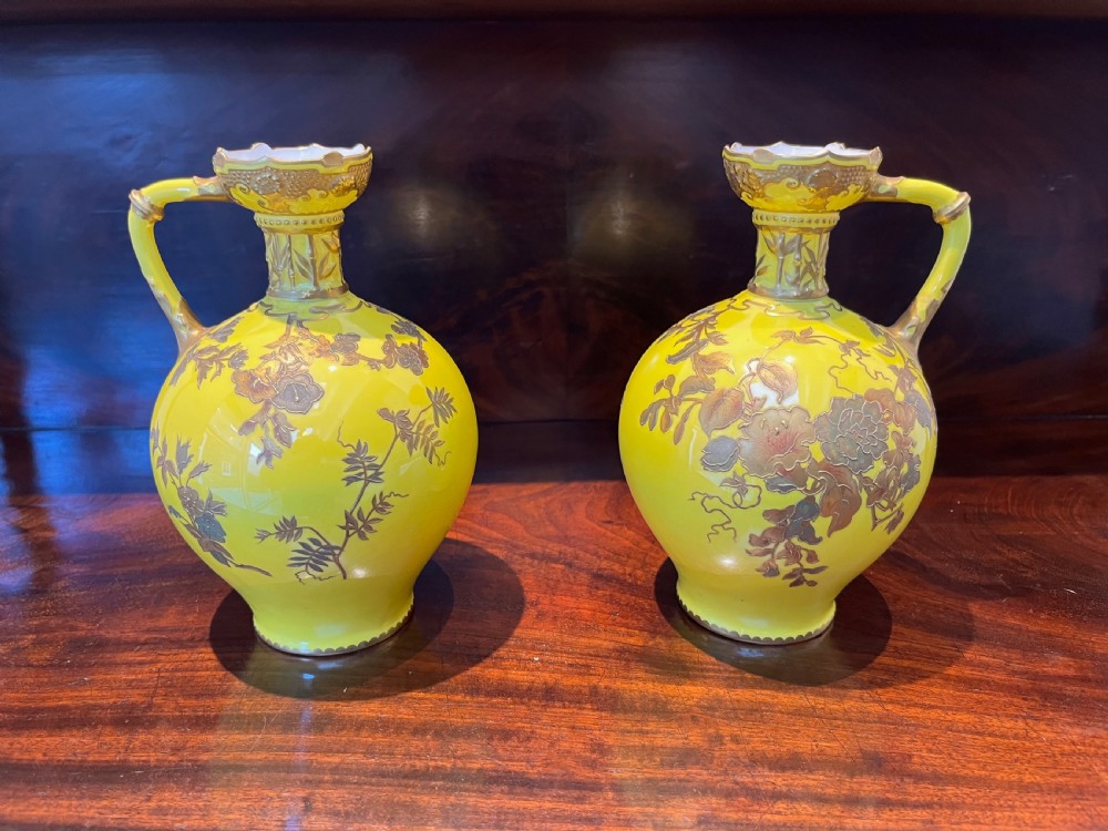 A pair of yellow porcelain ewers with gilded floral decoration, narrow necks, and single handles.