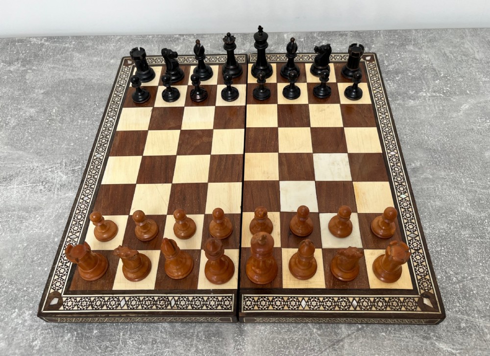 A wooden folding chess board featuring geometric inlaid borders and a full set of light and dark Staunton style chess pieces. View II
