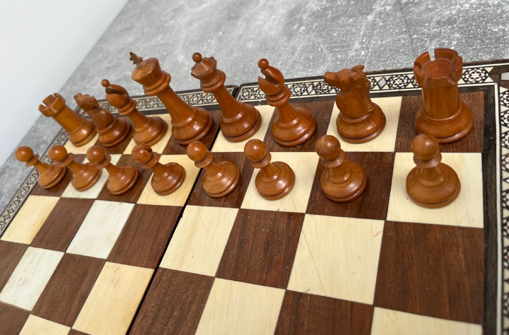 A wooden folding chess board featuring geometric inlaid borders and a full set of light and dark Staunton style chess pieces. View IV
