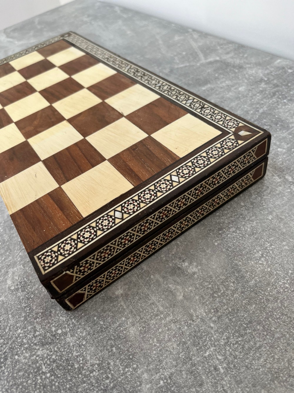 A wooden folding chess board featuring geometric inlaid borders and a full set of light and dark Staunton style chess pieces. View IX