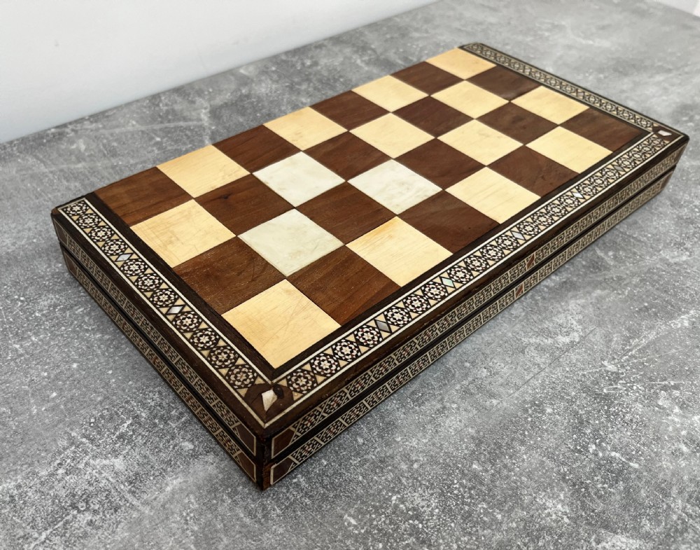 A wooden folding chess board featuring geometric inlaid borders and a full set of light and dark Staunton style chess pieces. View X
