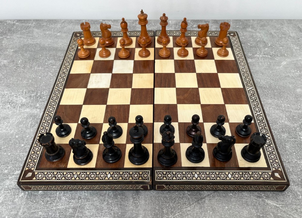 A wooden folding chess board featuring geometric inlaid borders and a full set of light and dark Staunton style chess pieces. View XIV