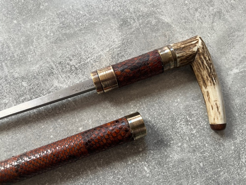 An antique French sword stick with a curved antler handle, brass collars, a narrow steel blade, and a sheath wrapped in dark brown snakeskin. View III