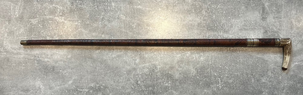 An antique French sword stick with a curved antler handle, brass collars, a narrow steel blade, and a sheath wrapped in dark brown snakeskin. View XV