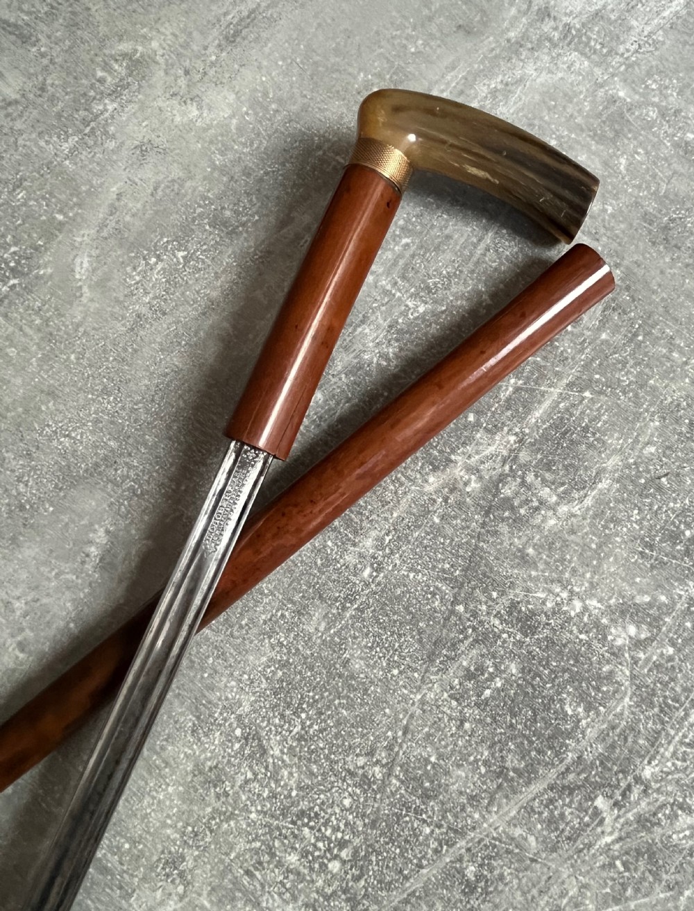 An antique French sword stick featuring an L-shaped horn handle, a gold-coloured engraved collar, a dark wooden sheath, and a slender unsheathed steel blade. View IV