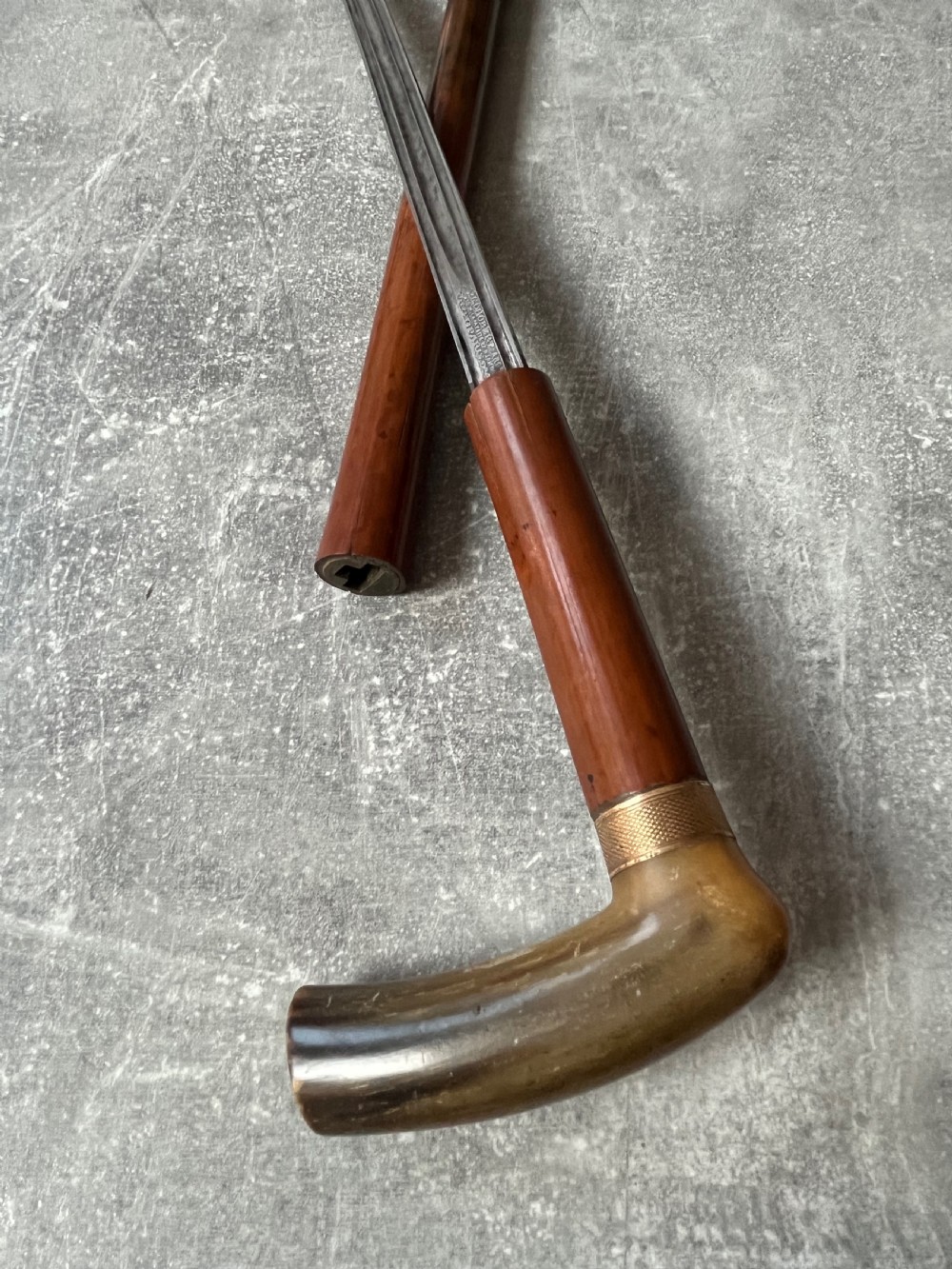 An antique French sword stick featuring an L-shaped horn handle, a gold-coloured engraved collar, a dark wooden sheath, and a slender unsheathed steel blade. View V
