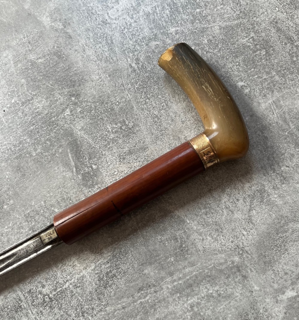 An antique French sword stick featuring an L-shaped horn handle, a gold-coloured engraved collar, a dark wooden sheath, and a slender unsheathed steel blade. View IX