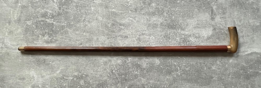 An antique French sword stick featuring an L-shaped horn handle, a gold-coloured engraved collar, a dark wooden sheath, and a slender unsheathed steel blade. View XII