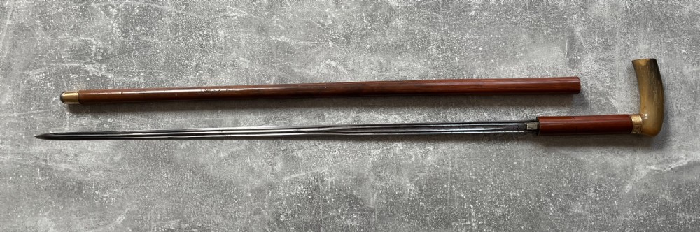 An antique French sword stick featuring an L-shaped horn handle, a gold-coloured engraved collar, a dark wooden sheath, and a slender unsheathed steel blade. View XIII