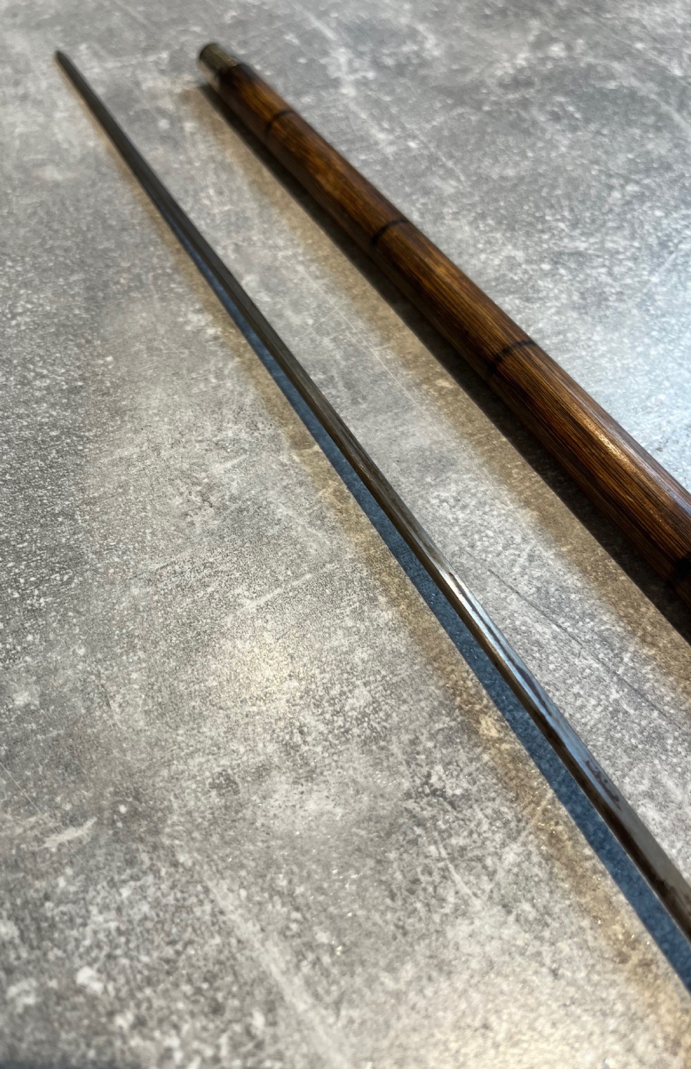 An antique Malacca walking stick unsheathed to reveal a long narrow steel sword blade, featuring a curved dark horn crook handle with a metal collar. View VIII