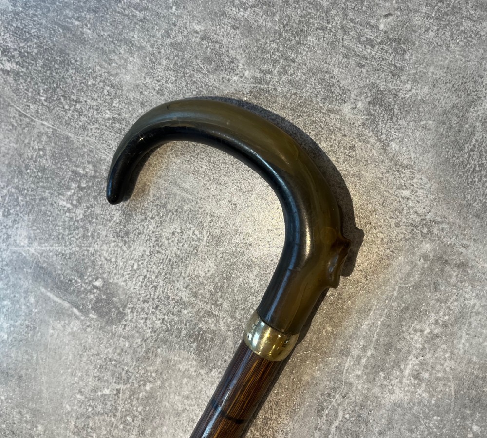 An antique Malacca walking stick unsheathed to reveal a long narrow steel sword blade, featuring a curved dark horn crook handle with a metal collar. View X