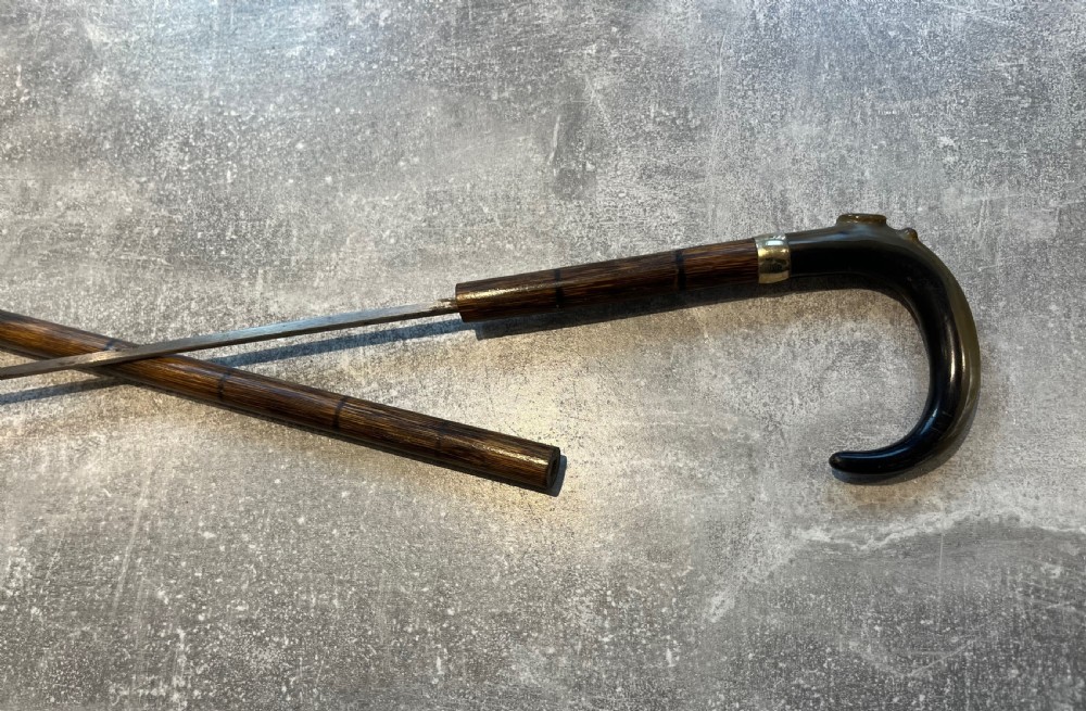 An antique Malacca walking stick unsheathed to reveal a long narrow steel sword blade, featuring a curved dark horn crook handle with a metal collar. View XI
