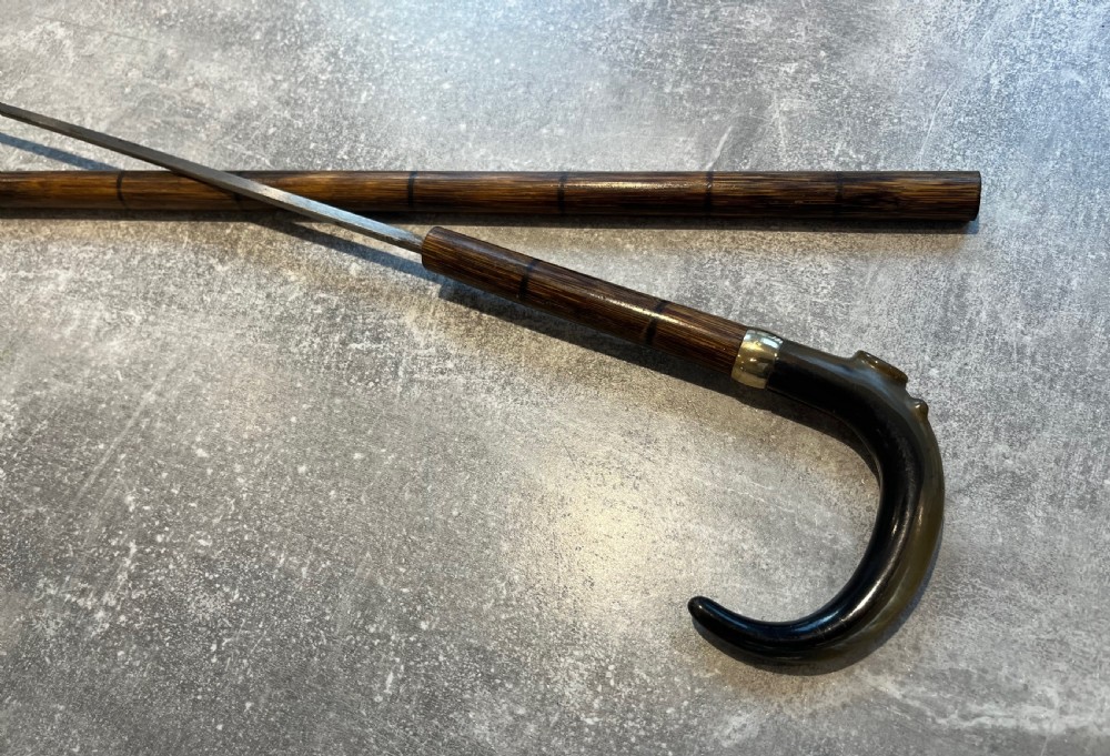 An antique Malacca walking stick unsheathed to reveal a long narrow steel sword blade, featuring a curved dark horn crook handle with a metal collar. View XIII