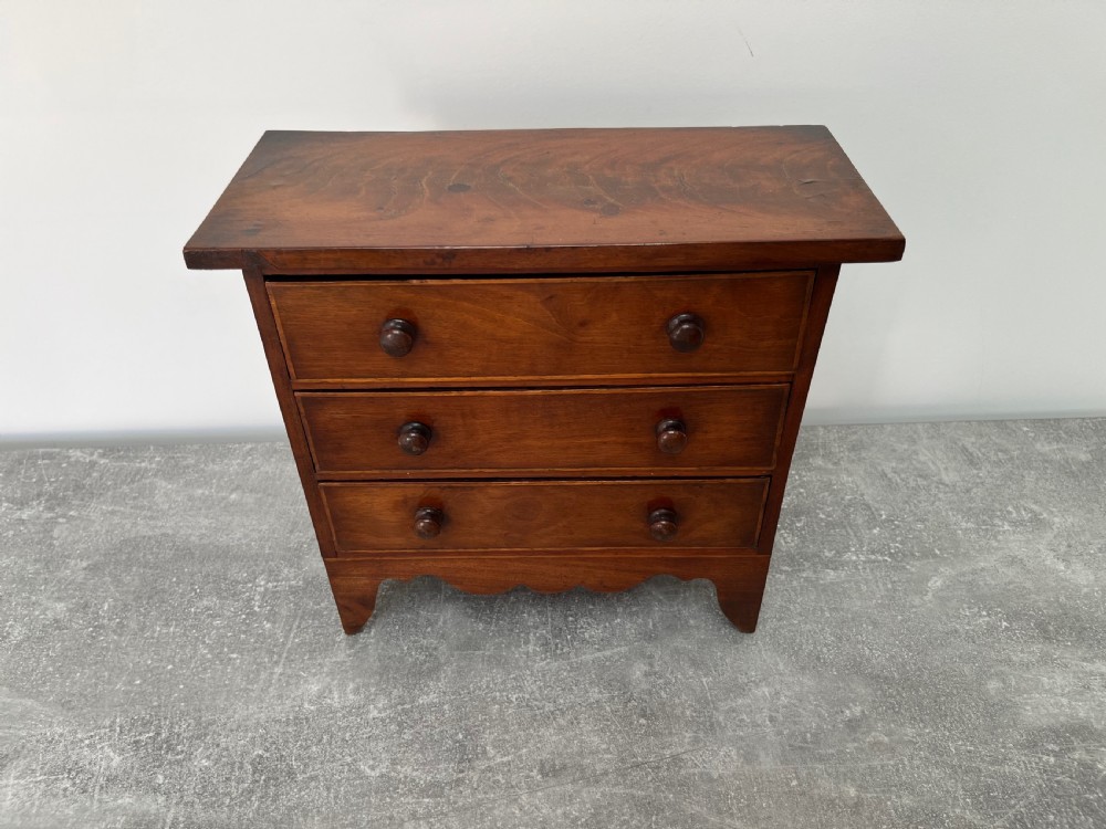 A miniature mahogany chest of drawers featuring three graduated drawers with turned wooden knobs and a shaped scalloped apron. View II
