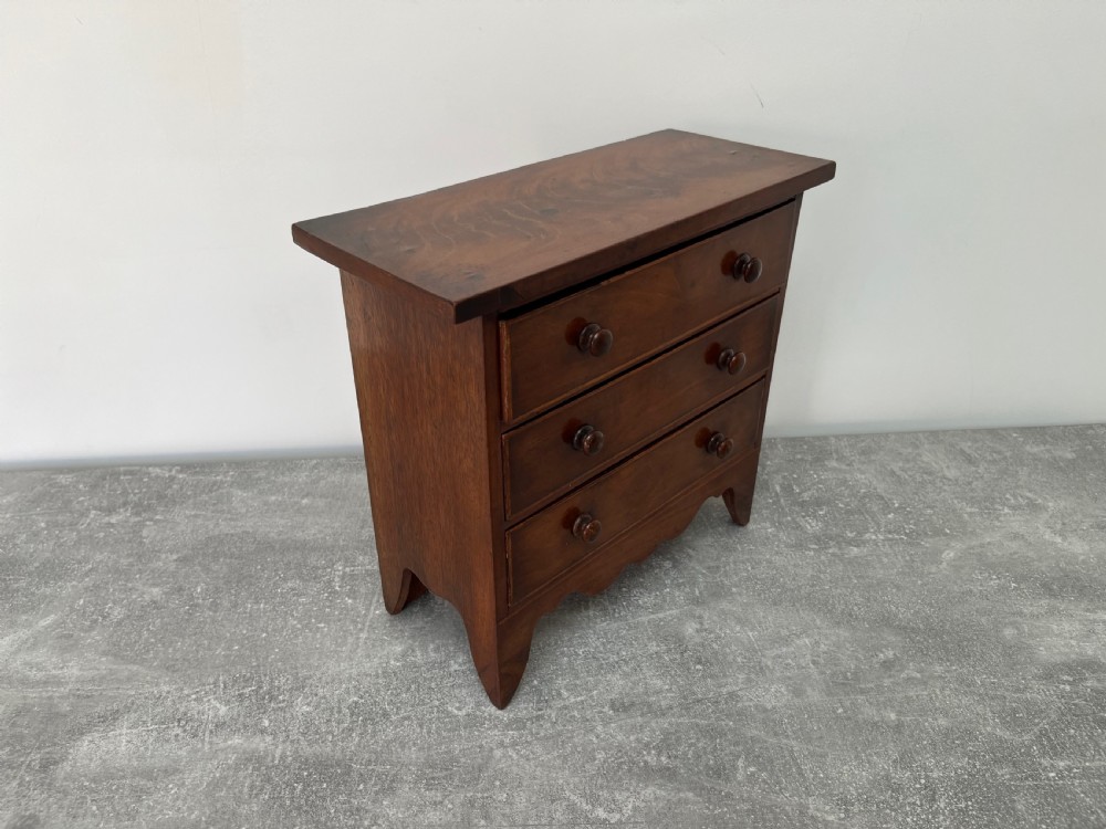 A miniature mahogany chest of drawers featuring three graduated drawers with turned wooden knobs and a shaped scalloped apron. View III