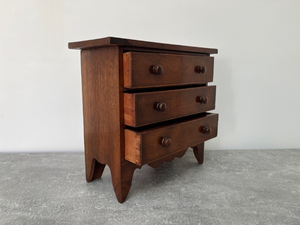 A miniature mahogany chest of drawers featuring three graduated drawers with turned wooden knobs and a shaped scalloped apron. View VII