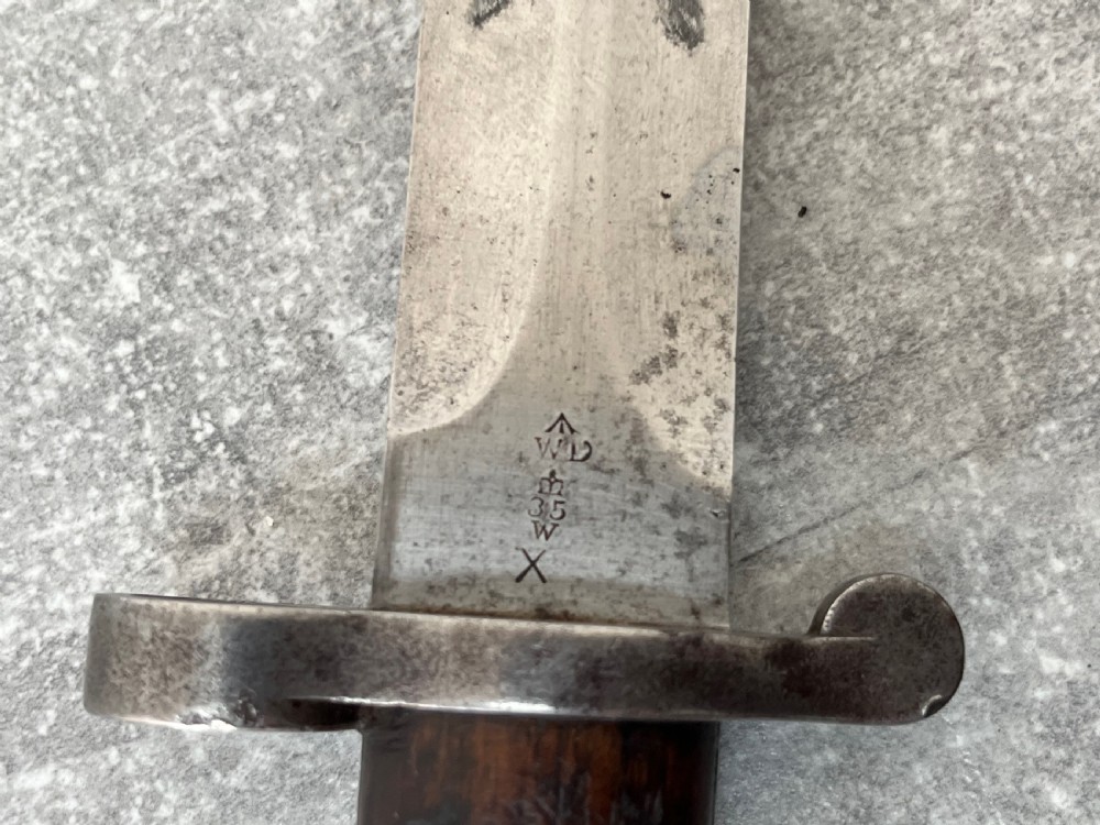 A Victorian British Pattern 1888 Mark 1 Type 2 sword bayonet with a double-edged steel blade, wooden handle grips secured with brass rivets, alongside its dark leather and steel-mounted scabbard. View V