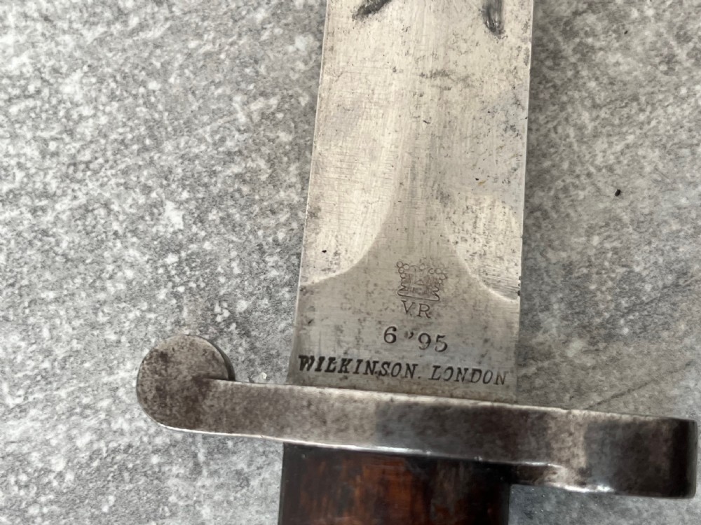 A Victorian British Pattern 1888 Mark 1 Type 2 sword bayonet with a double-edged steel blade, wooden handle grips secured with brass rivets, alongside its dark leather and steel-mounted scabbard. View VII