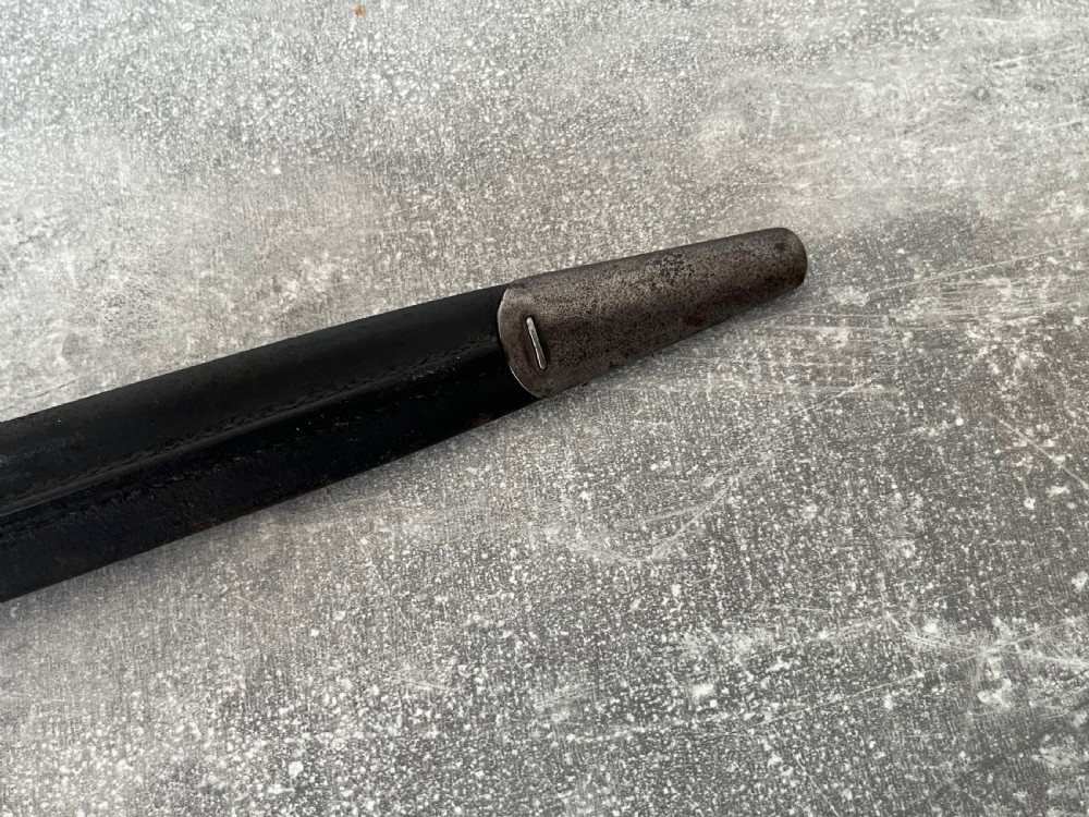 A Victorian British Pattern 1888 Mark 1 Type 2 sword bayonet with a double-edged steel blade, wooden handle grips secured with brass rivets, alongside its dark leather and steel-mounted scabbard. View X