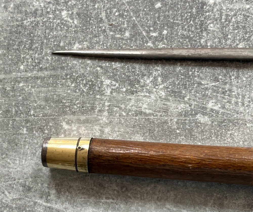 An antique chestnut wood sword stick shown unsheathed beside its shaft, featuring a root ball knob handle, silver collar mount, and long steel blade. View VII